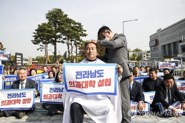 Rep. Kim Woni (C) from the main opposition Democratic Party holds a picket calling for the establishment of state-funded medical schools in South Jeolla Province, while his head is being shaved, on Oct. 18, 2023. (Pool photo) (Yonhap)