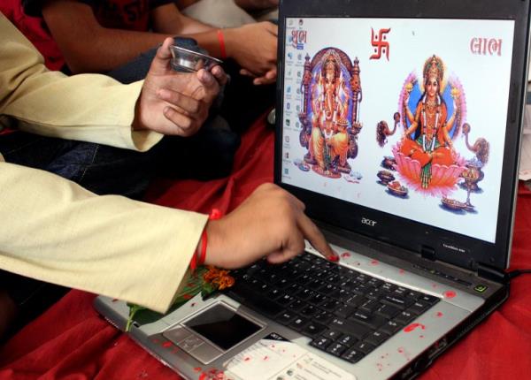 A businessman offers prayers to Hindu gods in front of a laptop as part of a ritual to worship the Hindu deity of wealth 